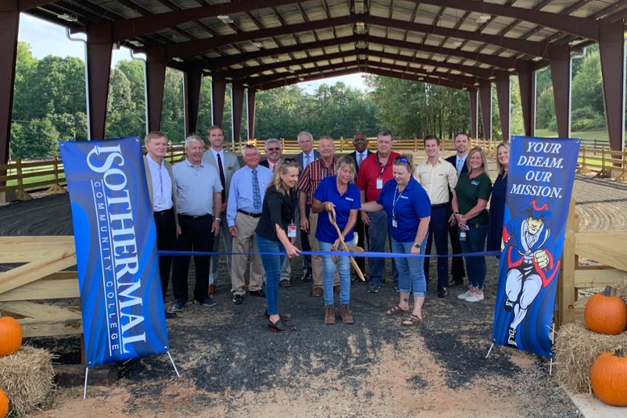 Ribbon cutting ceremony with equine instructors with scissors cutting a ribbon while surrounded by trustees and congressional representatives.