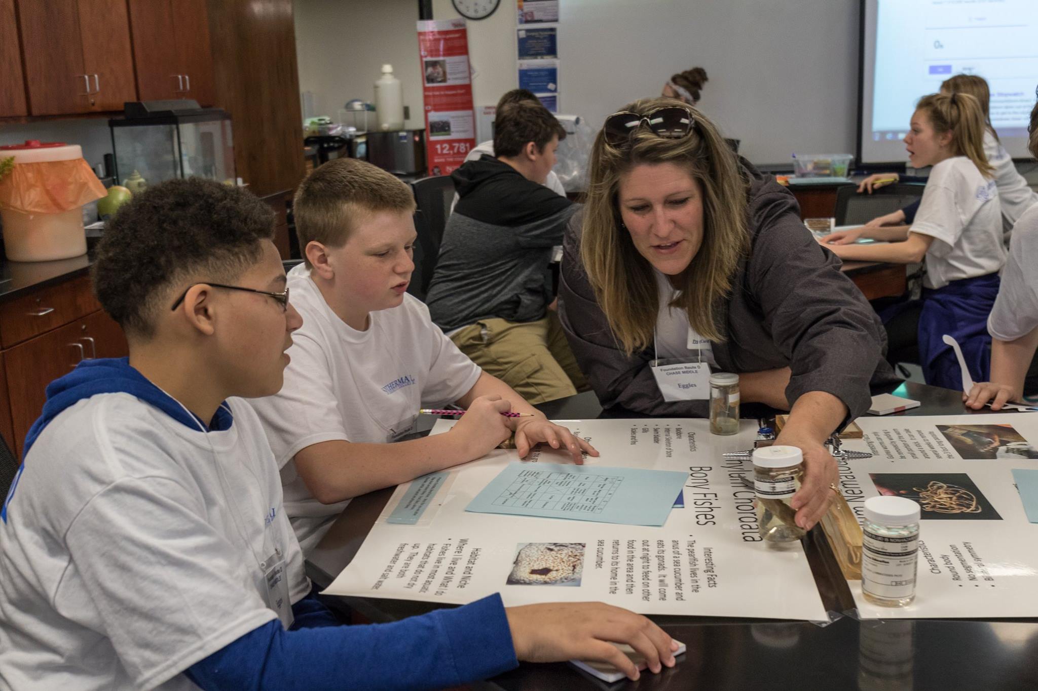 Teacher with  two students examining fish specimins in the biology lab 