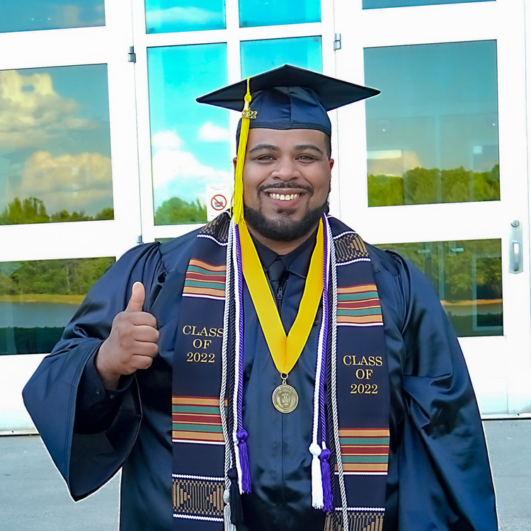 Jamor Logan, Sr., holding thumbs up wearing commencement regalia.