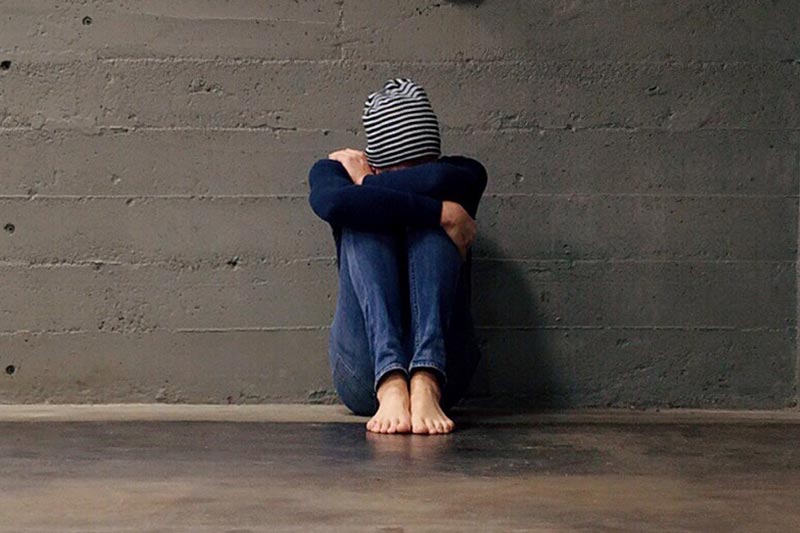 Person sitting alone with head tucked  in arms