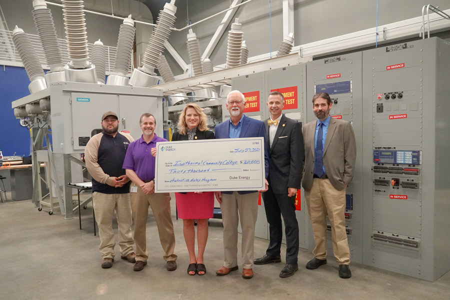 Representatives from Duke Energy Foundation and Isothermal holding oversized check in front of large substation equipment.