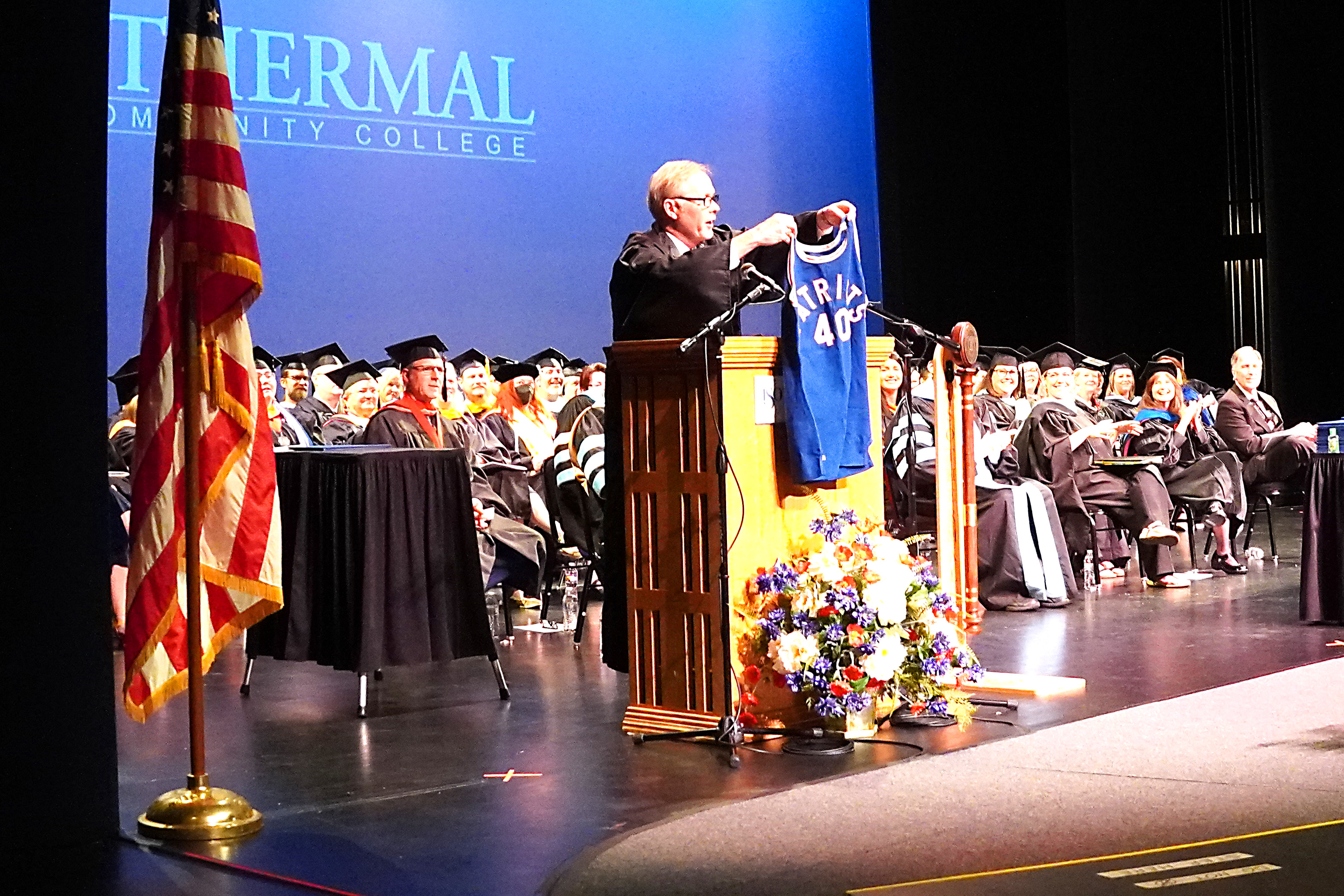 Bill McBrayer holding basketball jersey from the lecturn