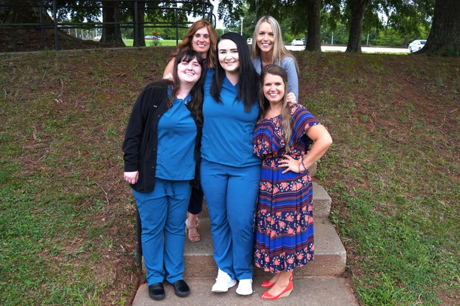 Two students in scrubs with three dental instructors on steps.