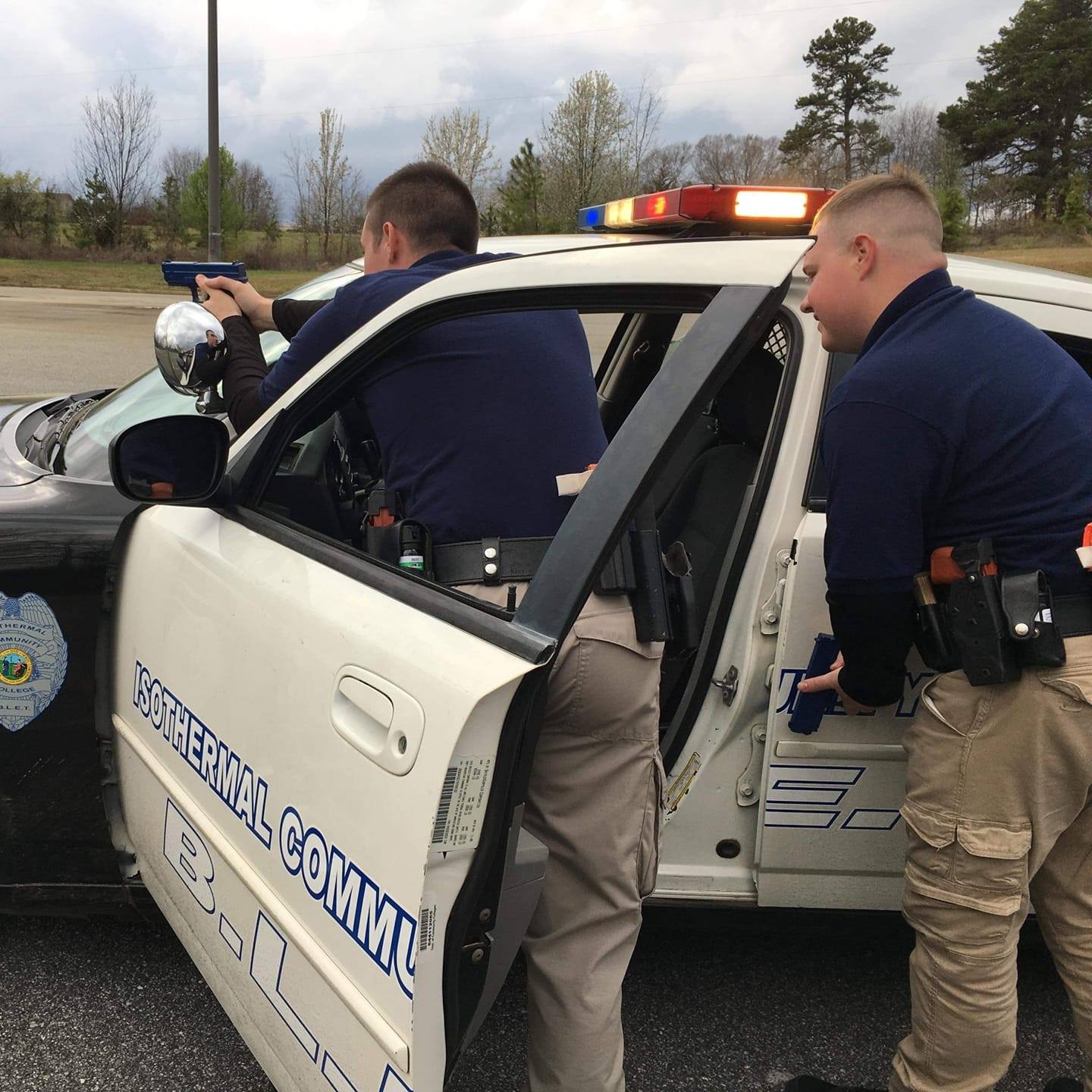 Two BLET students practice defensive positions behind car door.