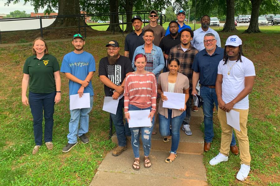 Graduates standing in group outdoors with certificates