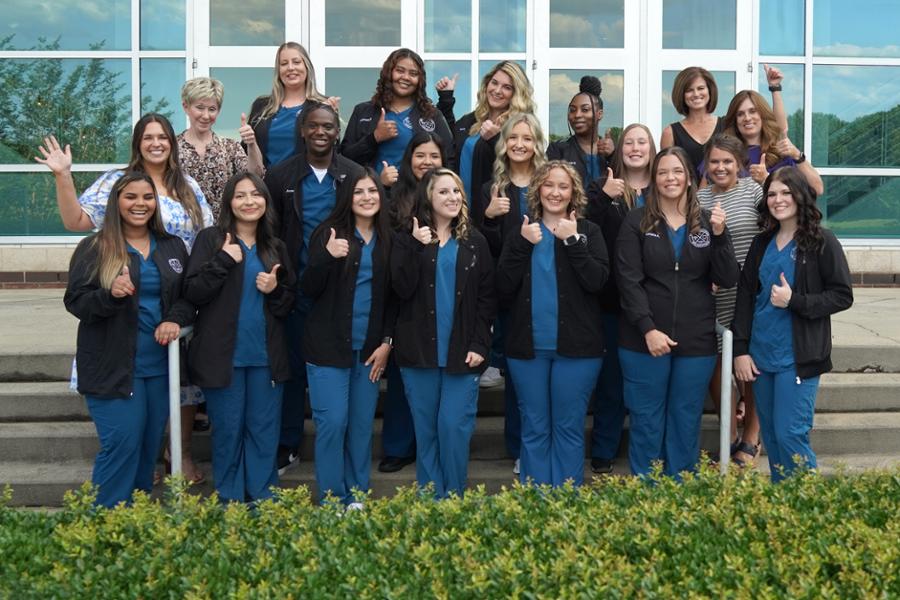 Dental assisting graduates in scrubs on steps in a large group