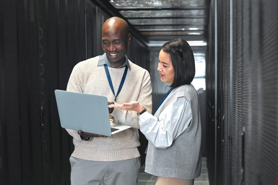 stock art of a male and female discussing around a laptop in a server room.