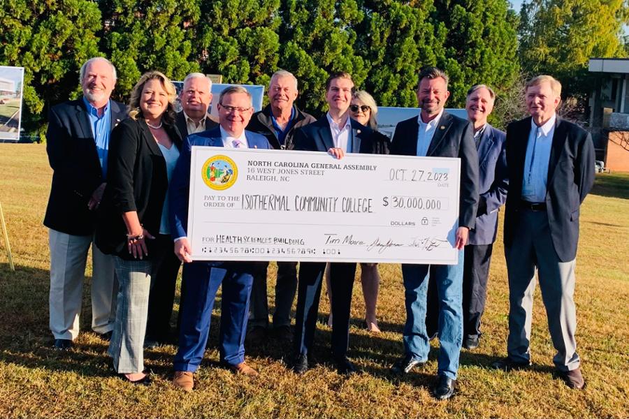 Legislators with officials from ICC holding oversized check at the location where new building will be built.