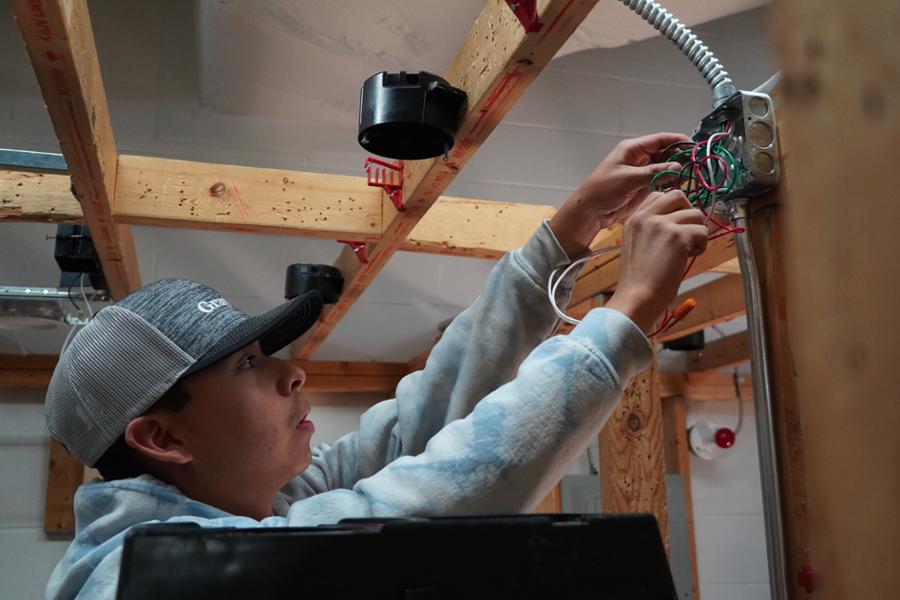 Student wiring an electrical junction box for an overhead light.