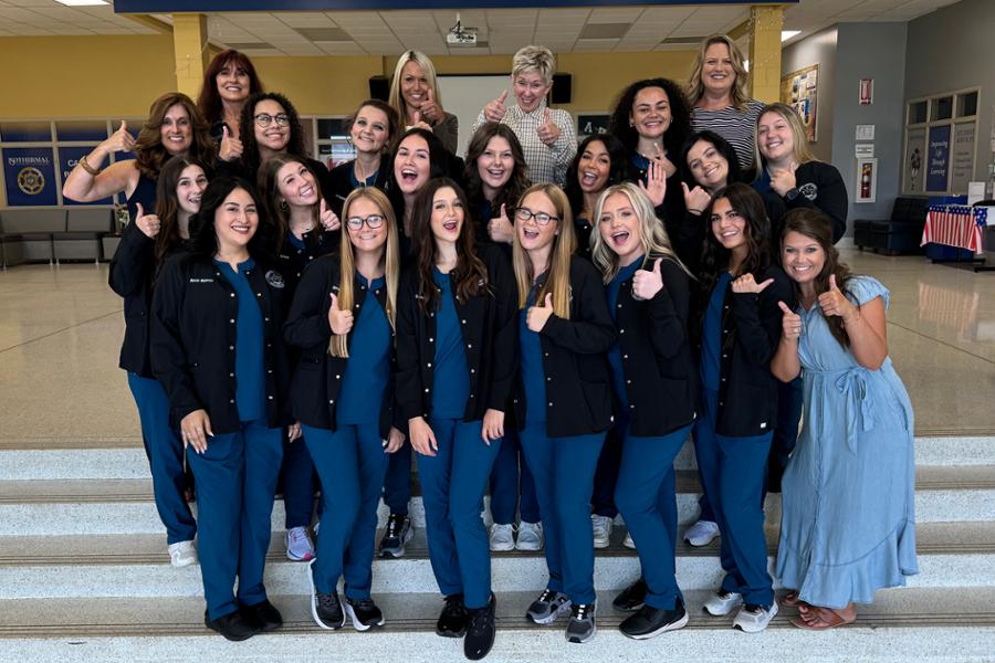All dental assisting students and instructors standing on steps giving a thumbs up