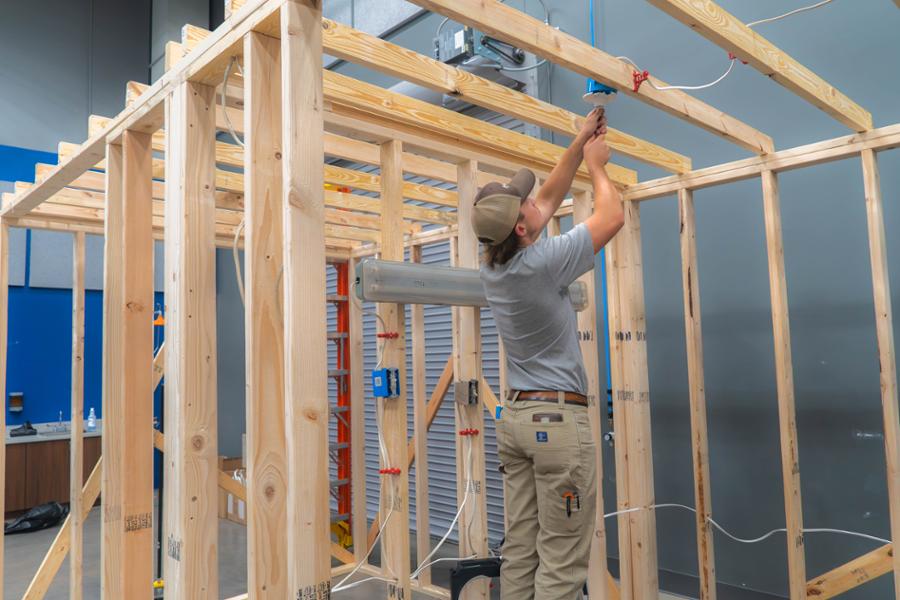 Student on ladder installing electrical connections in open-wall framing