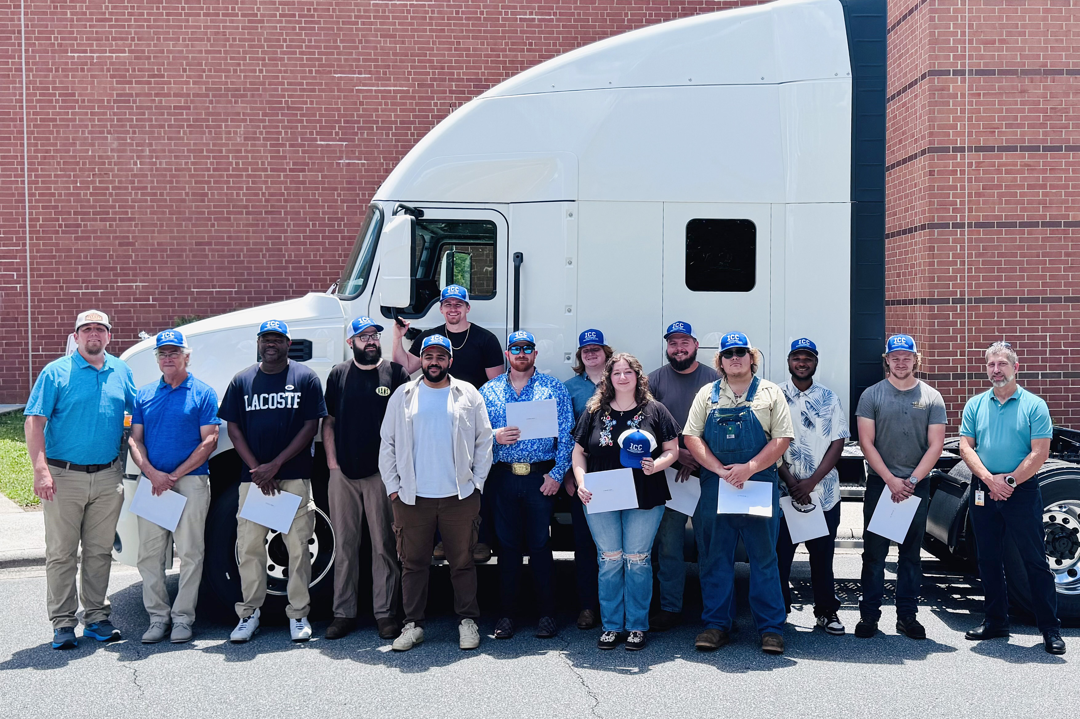 Twelve truck driving class graduates posing in front of a truck