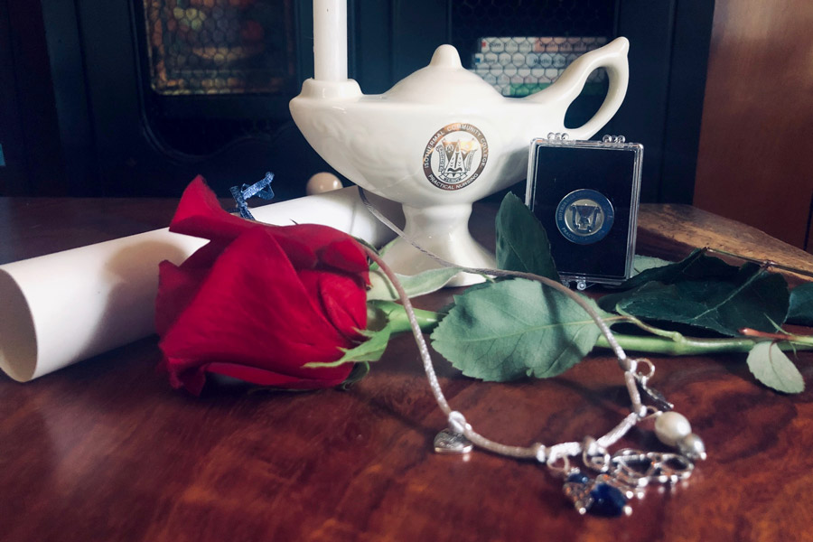 Practical Nursing Lamp and Pin on table with flowers, necklace, and rolled up diploma.